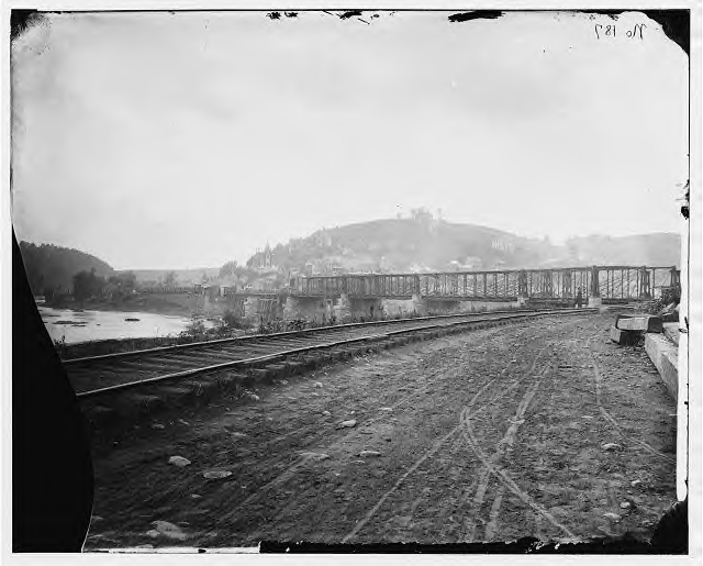 The bridge into Harpers Ferry before its first destruction. The track on the left, and on the bridge belongs to the Baltimore & Ohio RR. Track out of sight to the right, which joined the B&O track at the entrance to the bridge, belonged to the Winchester RR. Notice the ties are placed right on the ground.