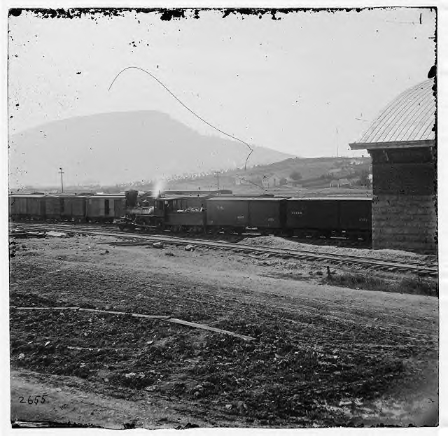 Good view of a locomotive, tender and box cars. Picture taken in Chattanooga in 1864 (Lookout Mountain is in the distance).